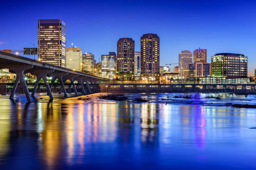 Ein Fluss spiegelt die Lichter einer beleuchteten Skyline und einer Brücke im Abendlicht wider.