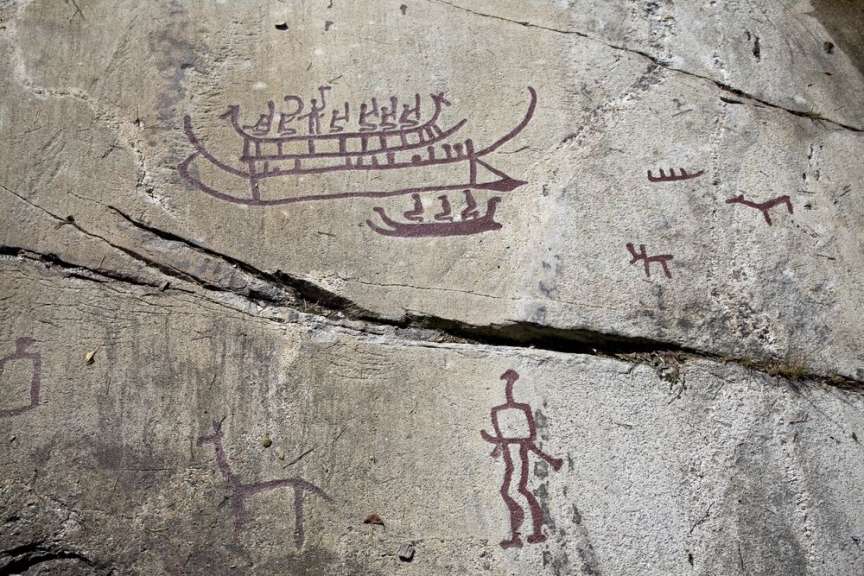 Auf einem Felsen sind Felszeichnungen von Schiffen, Menschen und Tieren zu sehen.