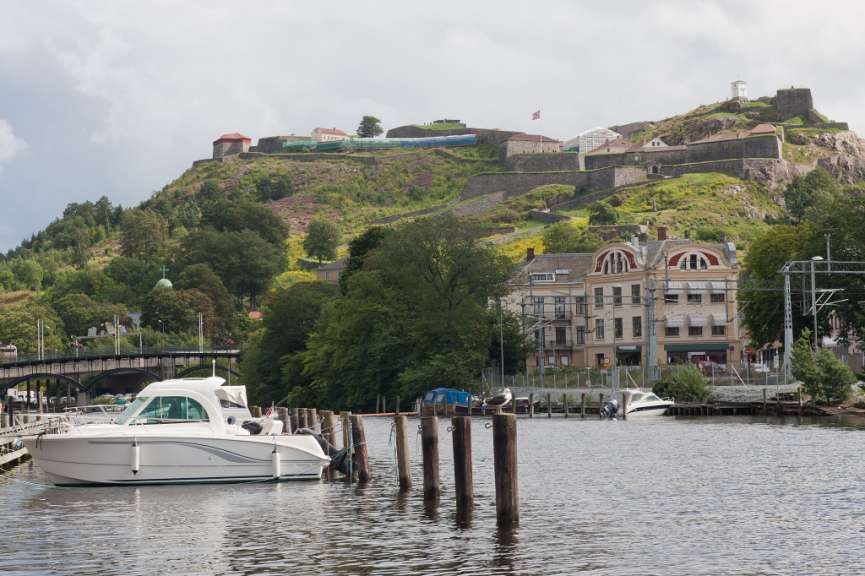 Ein breiter Fluss fließt an einer Festung auf einem Hügel vorbei, an dessen Ufer Häuser und Boote liegen.