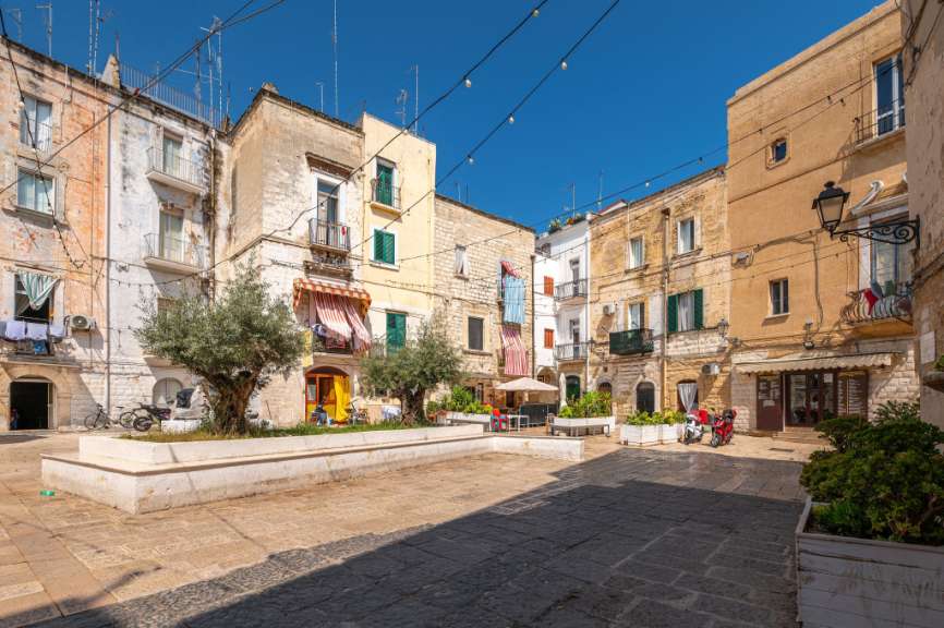 Ein sonniger Tag in einer italienischen Stadt mit Gebäuden, Olivenbäumen und einem Platz.