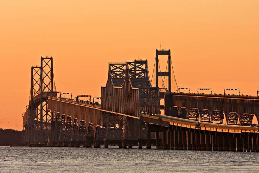Eine lange Brücke mit Autos darauf wird im Abendlicht vor einem orangen Himmel gezeigt.