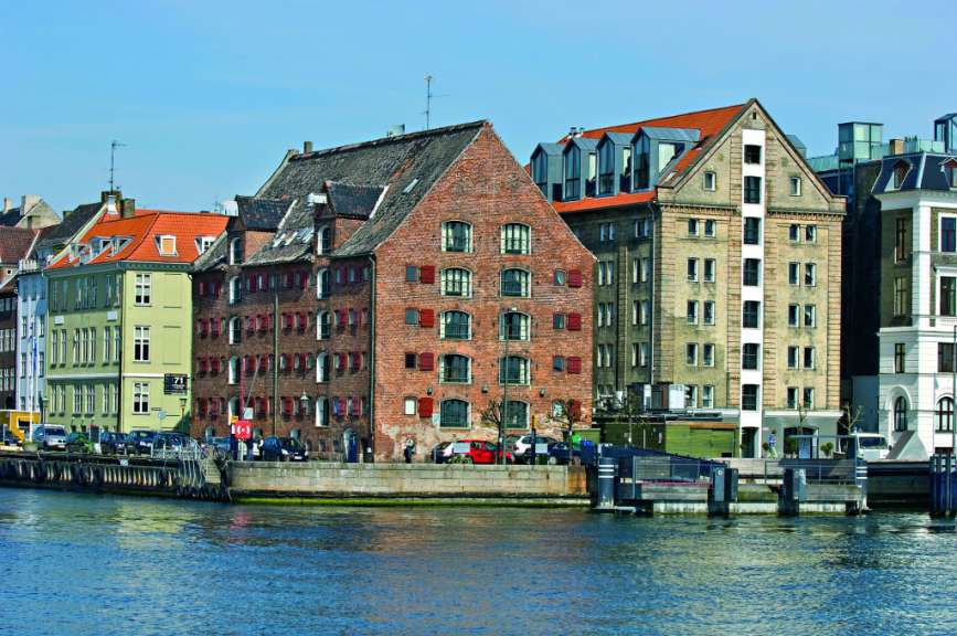 Ein Flussufer mit alten Backsteingebäuden und modernen Anbauten.