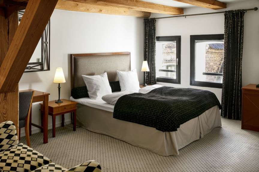 Ein gemütliches Hotelzimmer mit einem großen Bett, zwei Nachttischen und einem Schreibtisch ist in warmen Holztönen gehalten.