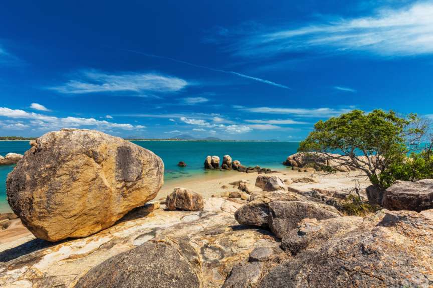 Ein Strand mit Felsen und Bäumen und einem großen Felsen im Vordergrund