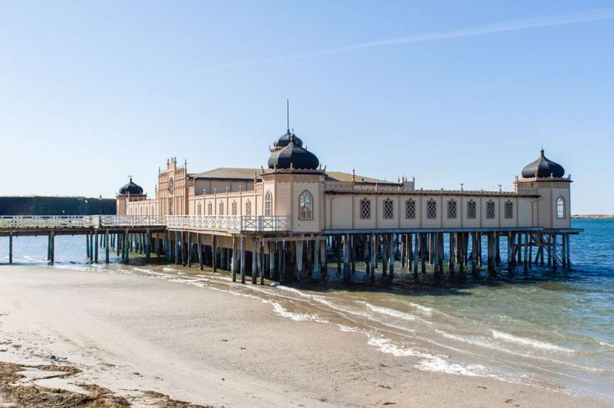Ein großes Gebäude auf Stelzen steht über einem Strand