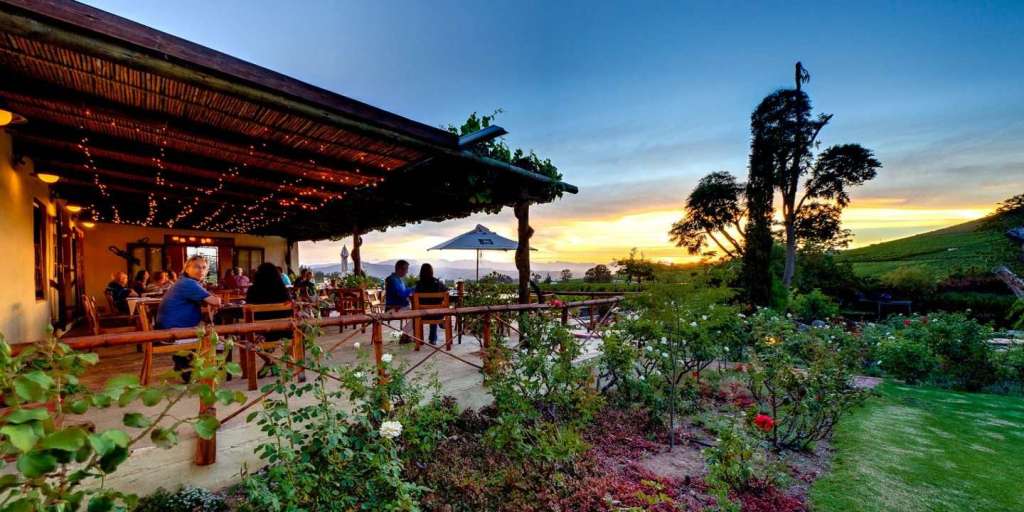 Eine Gruppe von Menschen sitzt auf einer Terrasse mit einem Sonnenuntergang im Hintergrund