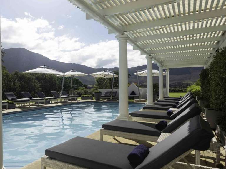 Liegestühle und Sonnenschirme um einen Pool mit Bergen im Hintergrund
