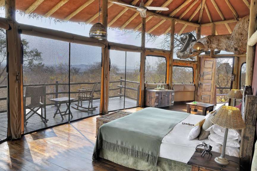 Das Bild zeigt ein luxuriöses Zelt-Schlafzimmer mit Blick auf die afrikanische Savanne.