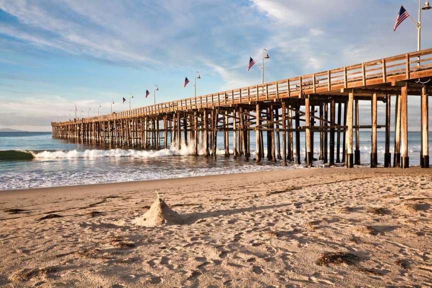Eine Sandburg steht am Strand vor einem Holzsteg