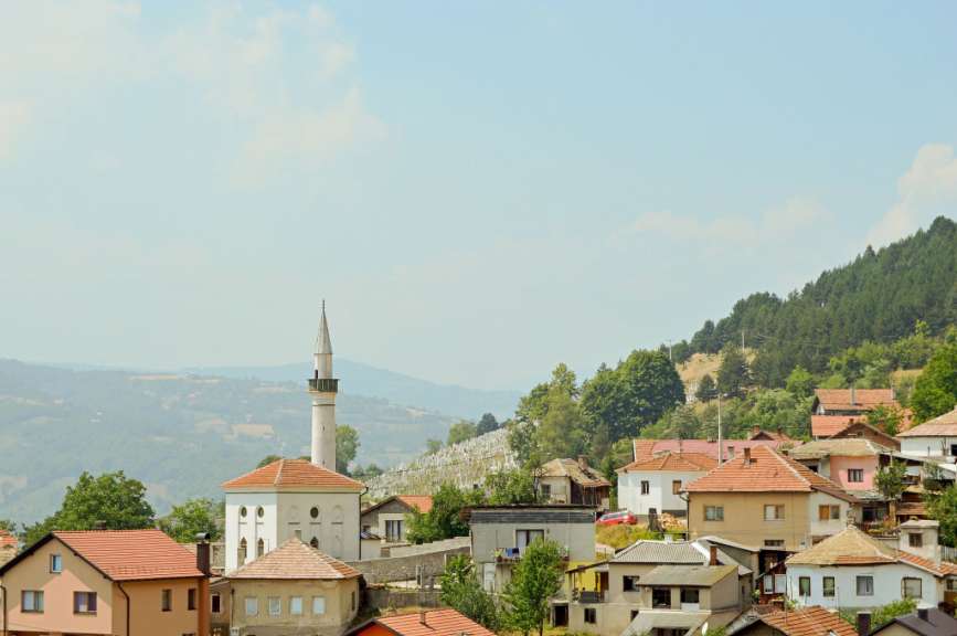 Eine Ansicht von Wohnhäusern und einer Moschee mit Minarett auf einem Hügel mit bewaldeten Hängen im Hintergrund.