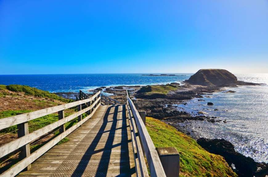 Eine Holzbrücke führt hinunter zu einem felsigen Strand