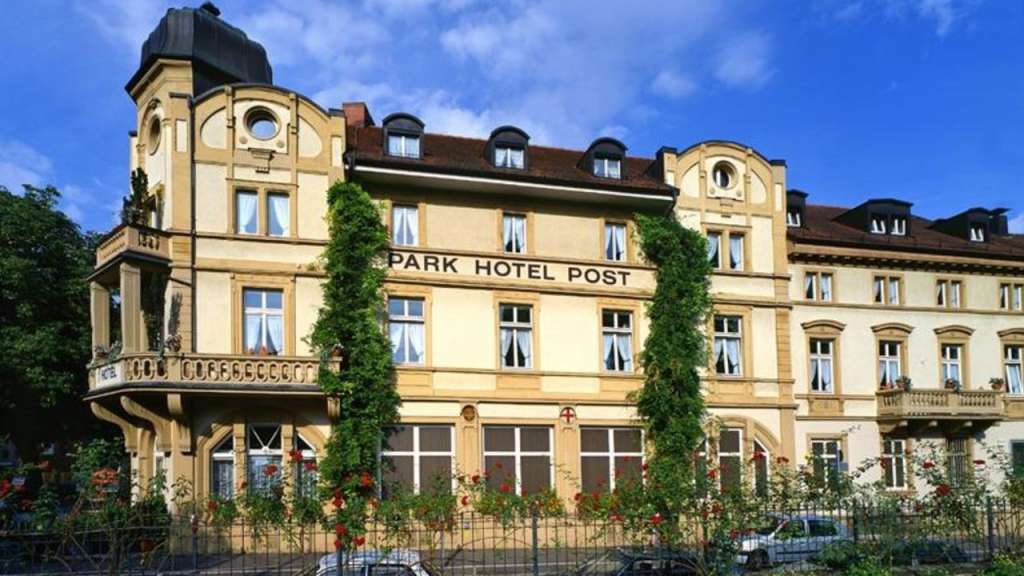 Ein altes Gebäude mit der Aufschrift "PARK HOTEL POST" vor einem blauen Himmel mit Wolken.