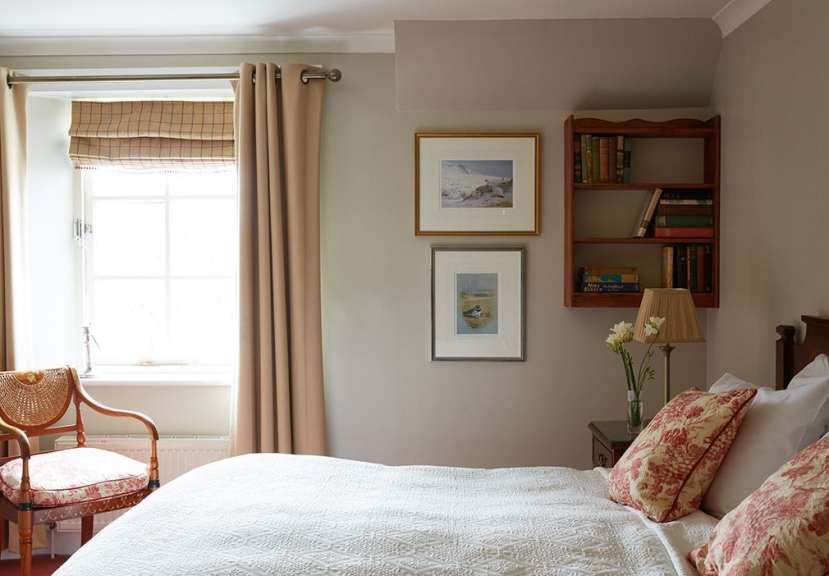Ein Schlafzimmer mit einem Bett, einem Stuhl, einem Fenster und einem Bücherregal.