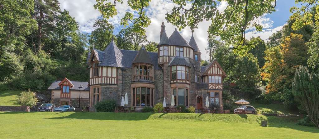 Ein großes Haus mit vielen Fenstern steht auf einem grünen Hügel