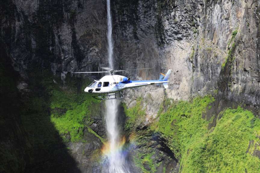 Ein weißer und blauer helikopter fliegt über einen wasserfall