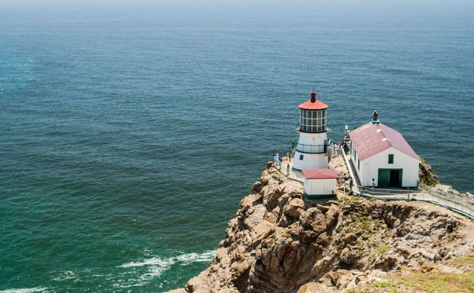 Ein Leuchtturm und ein Nebengebäude stehen auf einem felsigen Vorgebirge am Meer.