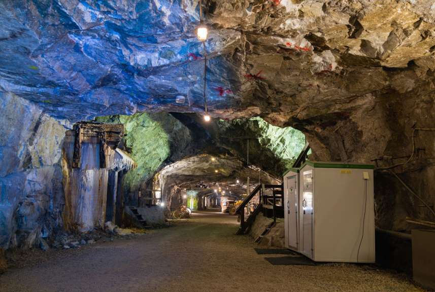 Ein beleuchteter unterirdischer Gang in einer Mine mit Felswänden, Ausrüstung und zwei weiß-grünen Kabinen.
