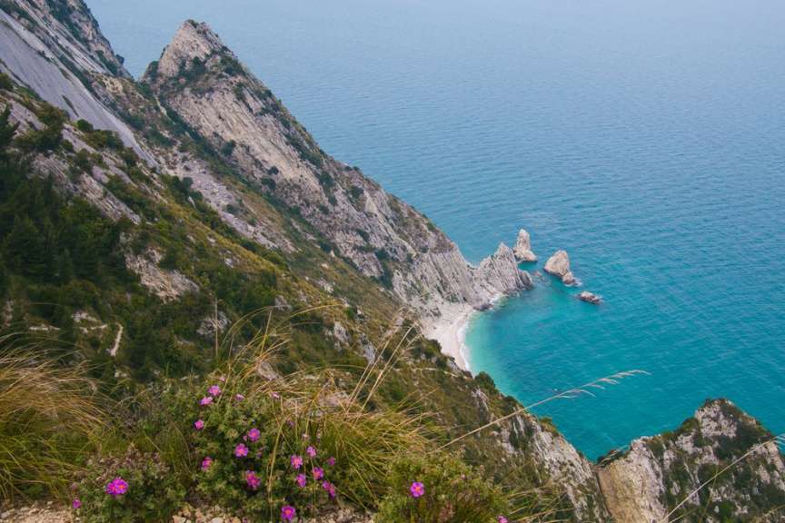 Das Bild zeigt eine felsige Steilküste mit üppiger Vegetation und einem türkisfarbenen Meer.