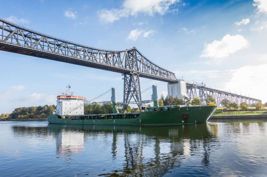 Ein grünes Schiff fährt unter einer Brücke über einen Fluss