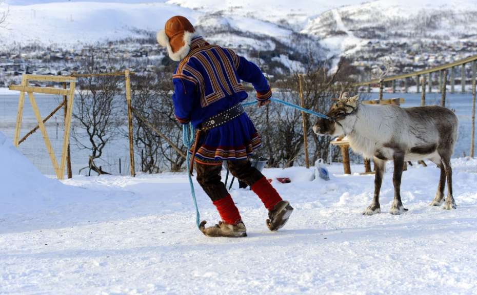 Ein Mann führt ein Rentier an der Leine durch den Schnee