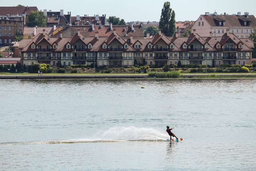Ein Mann wakeboardet auf einem See vor einer Reihe von Stadthäusern.