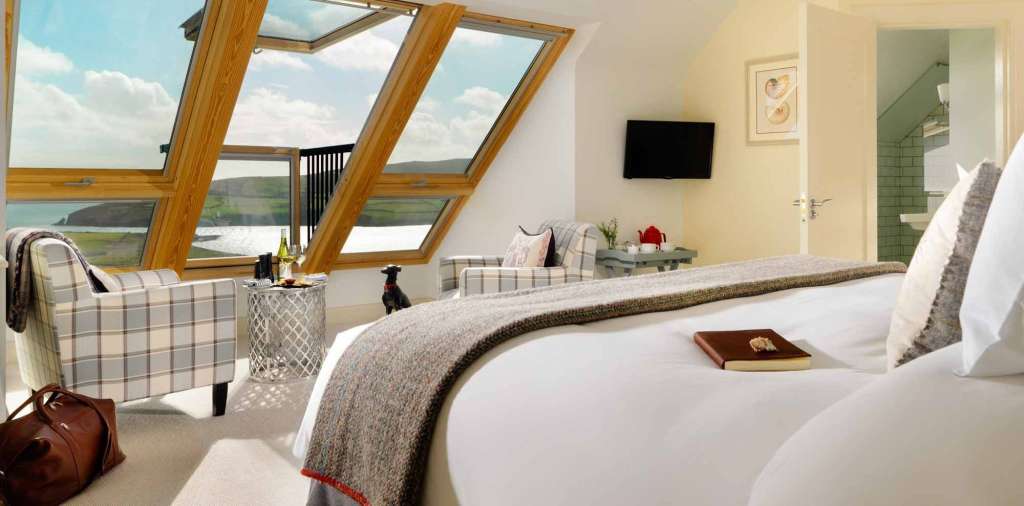 Ein stilvolles Schlafzimmer mit Dachfenstern, die einen malerischen Ausblick auf das Meer und die Landschaft bieten.