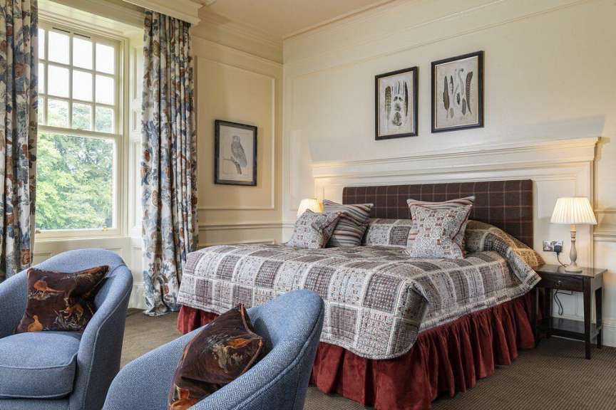Ein Schlafzimmer mit einem Bett, Sesseln, einem Fenster und Wanddekorationen.