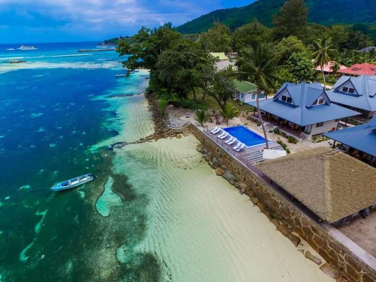 Eine Drohnenansicht zeigt eine luxuriöse Strandvilla mit Pool, die an einen tropischen Strand grenzt.