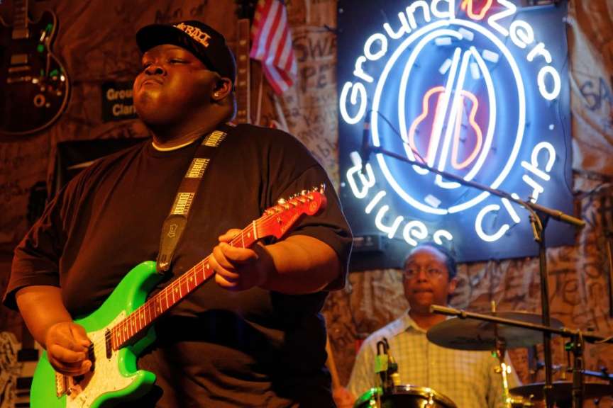 Ein Mann spielt eine grüne Gitarre vor einem Schild mit der Aufschrift ground zero blues club