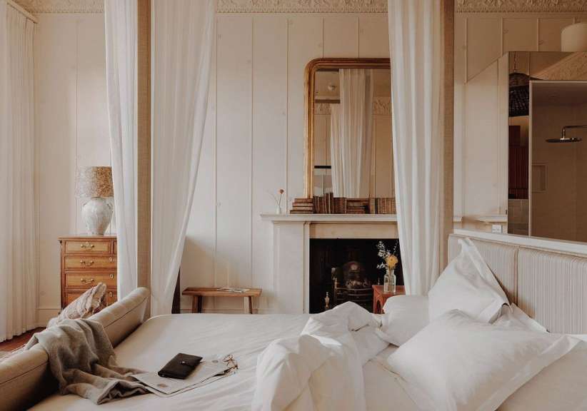 Ein luxuriöses Schlafzimmer mit einem Himmelbett und einem Kamin wird durch sanftes Licht erhellt.