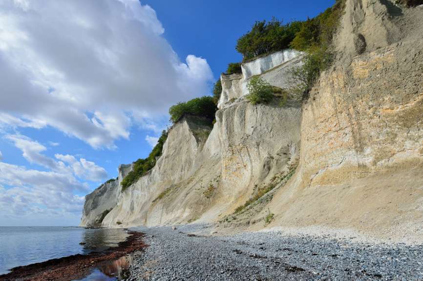 Eine Klippe mit Bäumen darauf steht über einem Kiesstrand