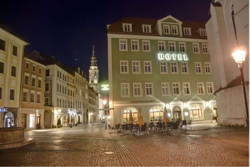 Eine Hotel- und Restaurantfassade mit leuchtender Beschriftung ist nachts in einer cobblestone Gasse zu sehen.