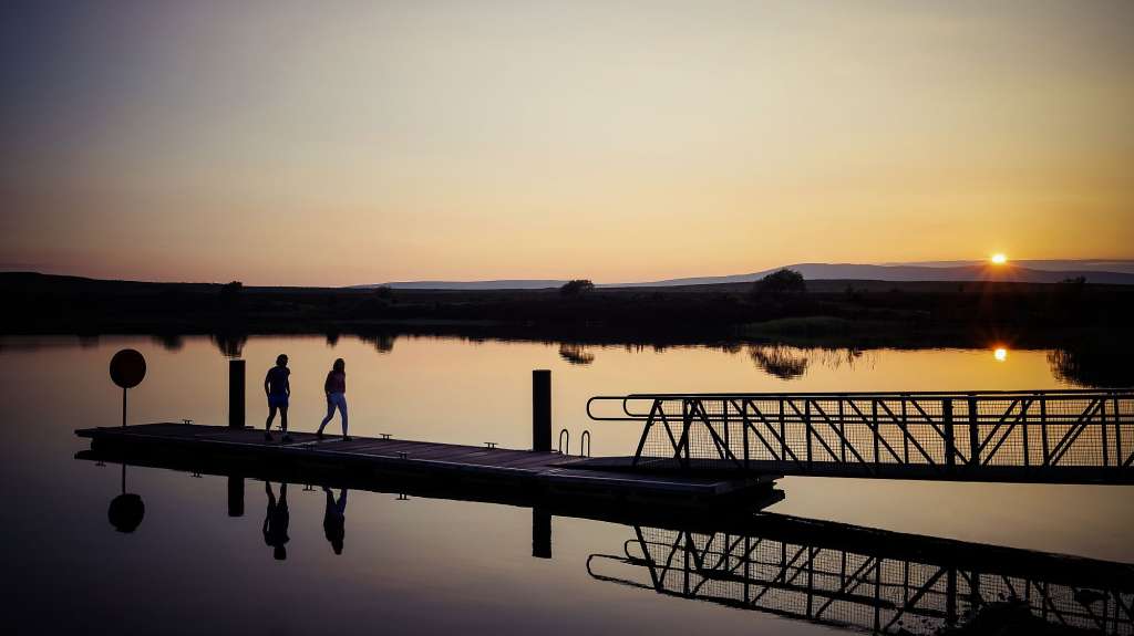 Menschen stehen auf einem Dock in einem See bei Sonnenuntergang