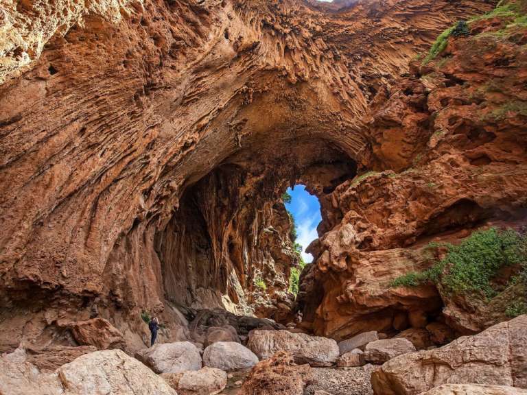 Ein Mann fotografiert eine imposante Felsformation mit einer Öffnung zum blauen Himmel in einem Canyon.