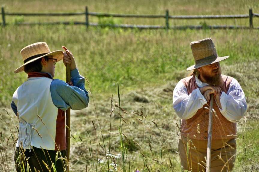 Zwei Männer in traditioneller Kleidung stehen auf einem Feld mit Werkzeugen.