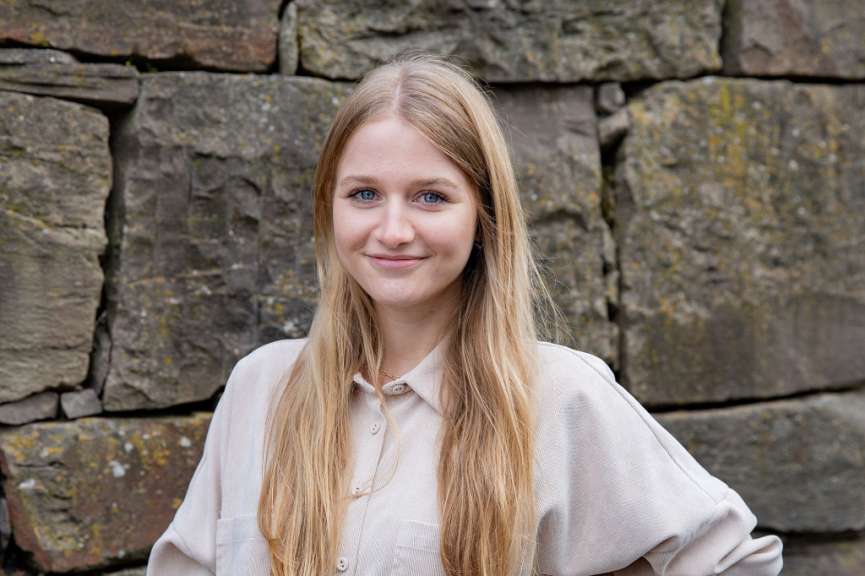 ©Barbara Harbecke Eine blonde frau steht vor einer steinmauer und lächelt