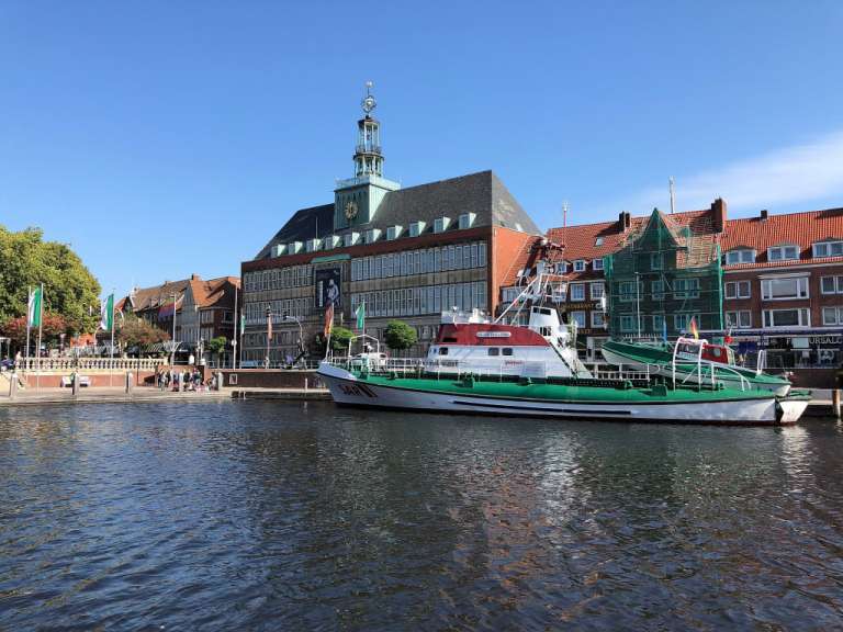 Ein Schiff liegt in einem Hafen vor einem Gebäude mit einem Glockenturm.