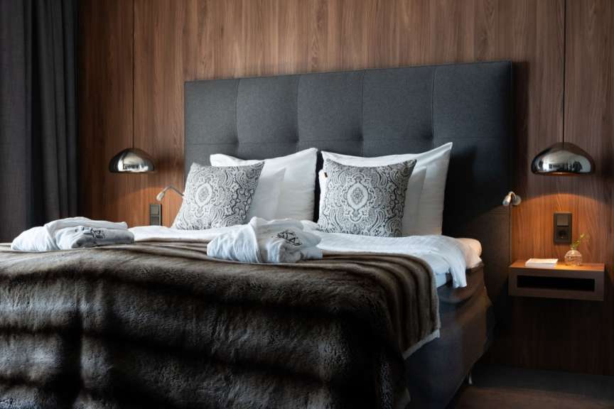 Ein luxuriös eingerichtetes Hotelzimmer mit einem großen Bett, dekorativen Kissen, einem flauschigen Überwurf und stilvollen Nachttischen.