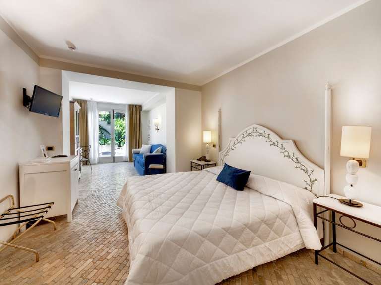 Ein luxuriöses Hotelzimmer mit einem großen weißen Bett, einem blauen Sofa und einer Tür, die auf einen Garten führt.