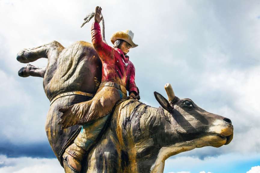 Eine Statue eines Cowboys auf einem Bullen vor einem bewölkten Himmel.