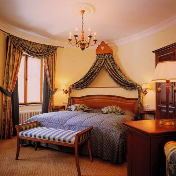 Ein luxuriöses Hotelzimmer mit einem Himmelbett, einer Sitzbank und einem Schrank.