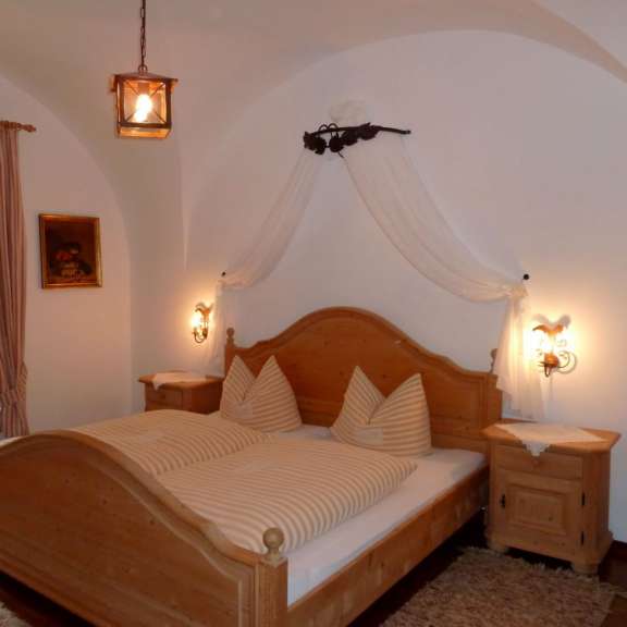 Ein Doppelbett mit gestreifter Bettwäsche und weißen Kissen steht in einem Raum mit einer Deckenbeleuchtung, einem Bild an der Wand und einem Nachttisch.