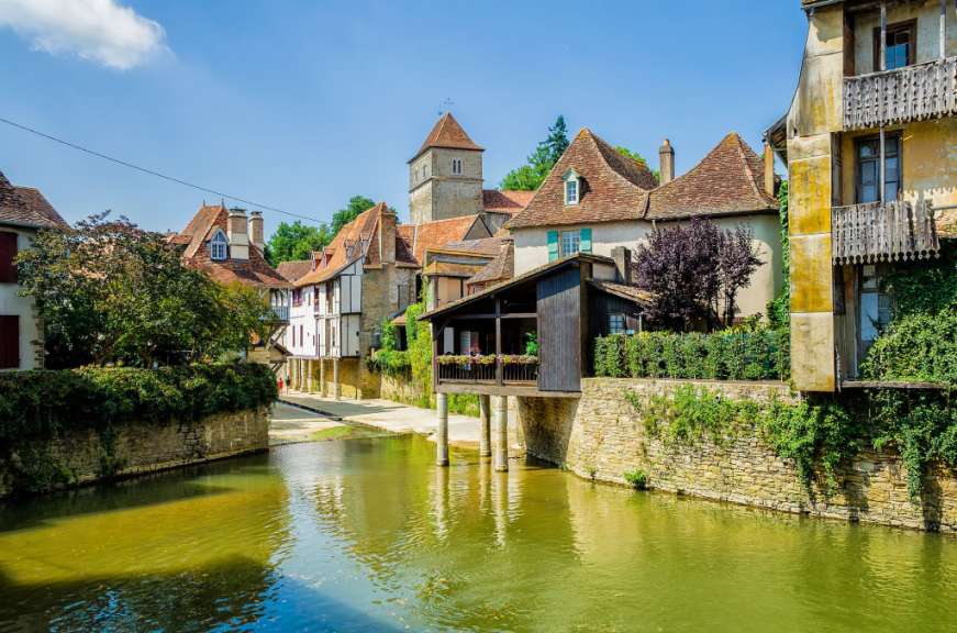 Ein malerisches Dorf mit Fachwerkhäusern und einem Fluss fließt unter ihnen hindurch.
