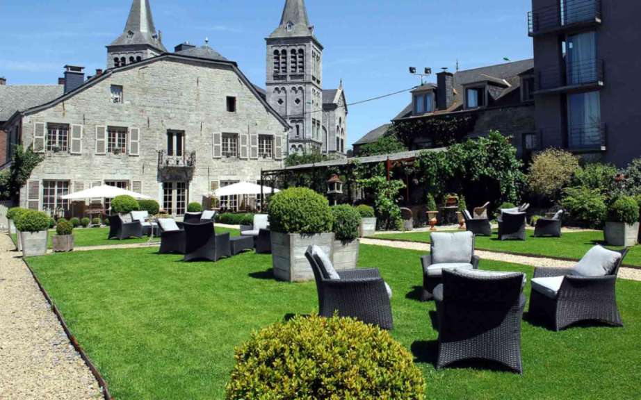 Ein Garten mit Rasen, Büschen und Sitzgelegenheiten, der von historischen Gebäuden und einem Kirchturm umgeben ist.