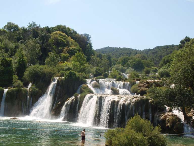 Ein Mann steht im Wasser vor einem Wasserfall