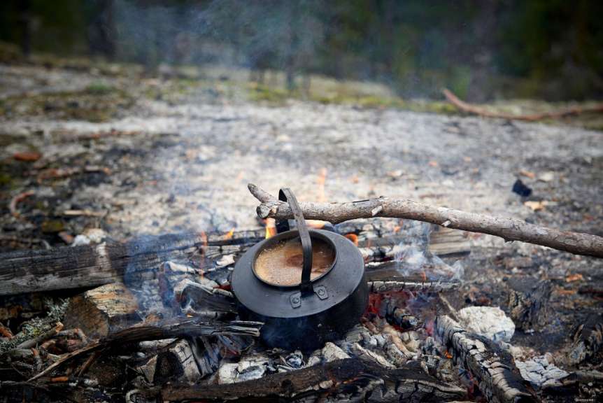 Eine schwarze Teekanne steht auf einem Lagerfeuer