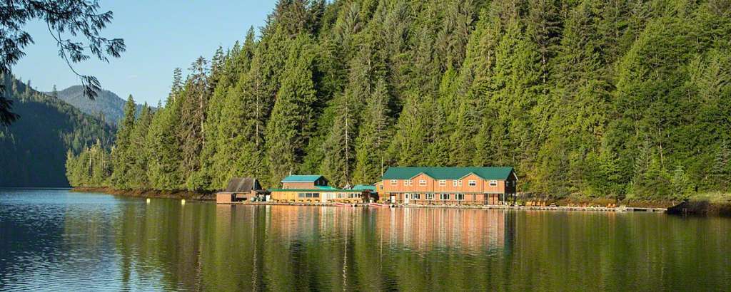 Ein auf dem Wasser schwimmender Gebäudekomplex ist von einem dichten, grünen Wald umgeben, der sich an einen bewaldeten Hang schmiegt.