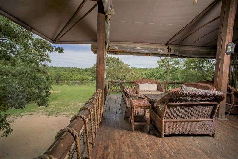 Auf einer Holzterrasse mit Blick auf eine grüne Landschaft und einen Teich stehen Korbmöbel.