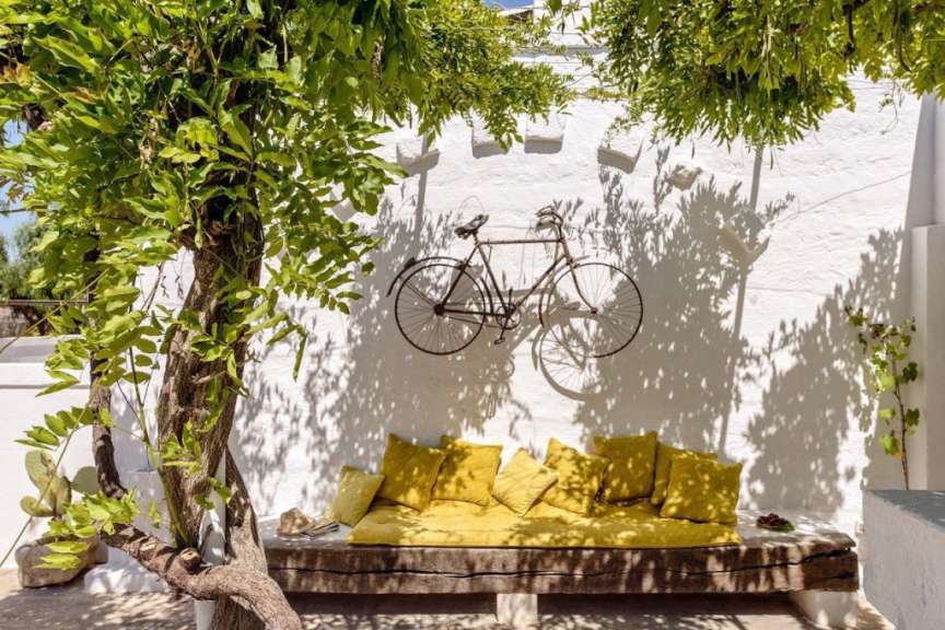 Ein Fahrrad hängt an einer weißen Wand neben einer Bank mit gelben Kissen