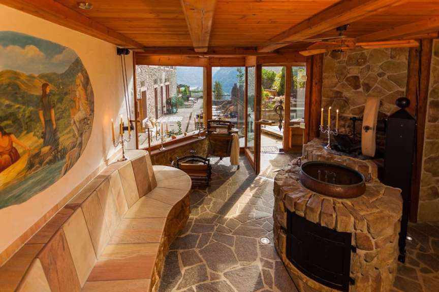 Eine sonnendurchflutete Veranda mit einem Kamin, Sitzbänken und Blick auf eine Berglandschaft.